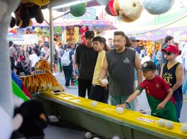 A diverse group of people engages in a fun carnival game, surrounded by vibrant festival activities.