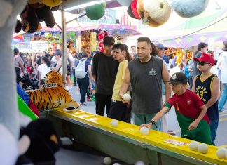 A diverse group of people engages in a fun carnival game, surrounded by vibrant festival activities.