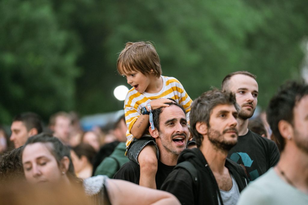 Joyful father with son on shoulders at an outdoor festival. Lively crowd enjoying the event.