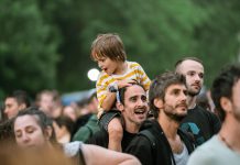 Joyful father with son on shoulders at an outdoor festival. Lively crowd enjoying the event.