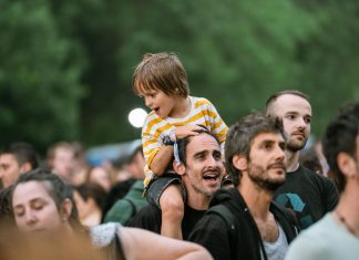 Joyful father with son on shoulders at an outdoor festival. Lively crowd enjoying the event.