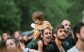Joyful father with son on shoulders at an outdoor festival. Lively crowd enjoying the event.