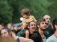 Joyful father with son on shoulders at an outdoor festival. Lively crowd enjoying the event.
