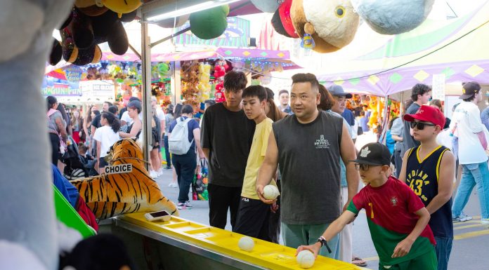 A diverse group of people engages in a fun carnival game, surrounded by vibrant festival activities.