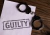 Top view of handcuffs on paper with 'GUILTY' text, symbolizing a verdict or crime.