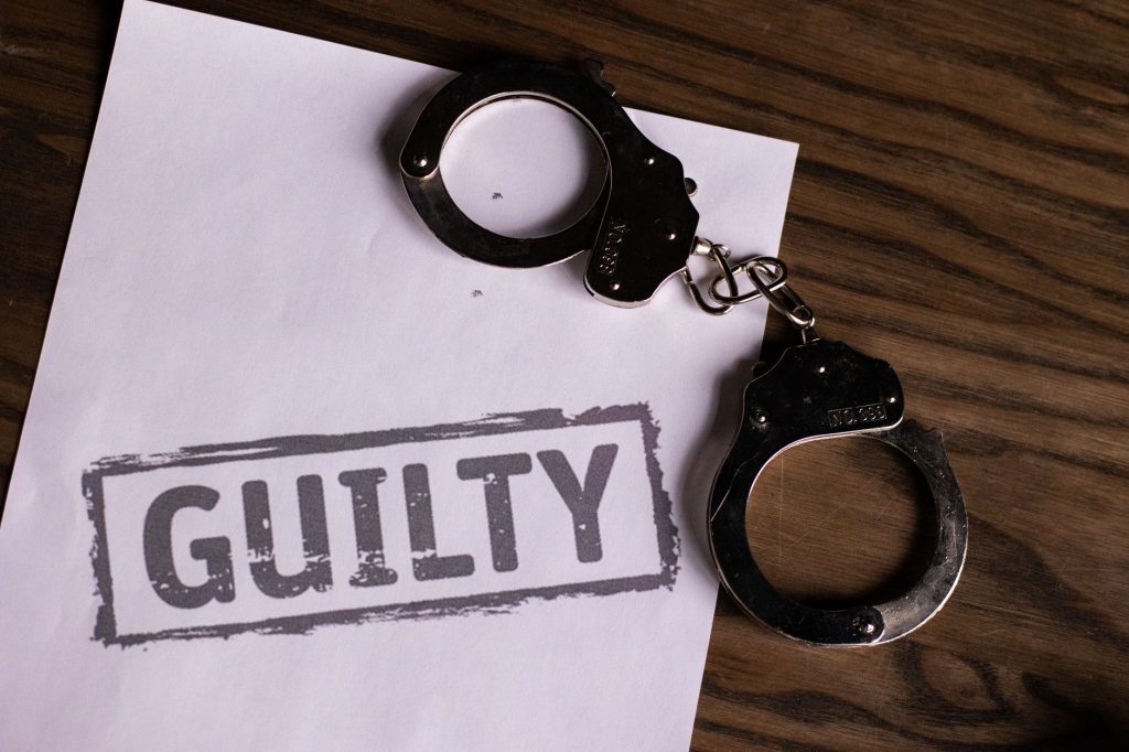 Top view of handcuffs on paper with 'GUILTY' text, symbolizing a verdict or crime.
