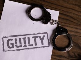 Top view of handcuffs on paper with 'GUILTY' text, symbolizing a verdict or crime.