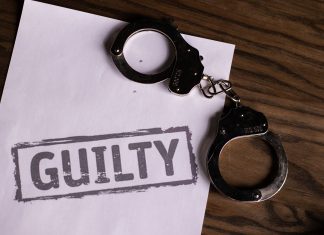 Top view of handcuffs on paper with 'GUILTY' text, symbolizing a verdict or crime.