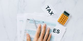 Close-up of a hand on tax form 1040 with a calculator on a desk.