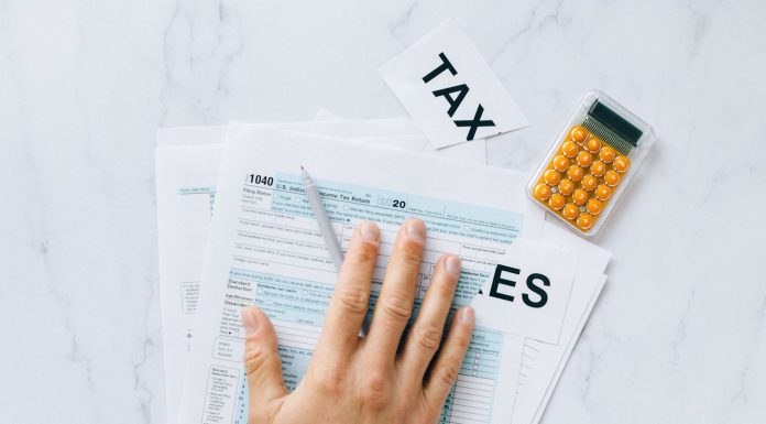 Close-up of a hand on tax form 1040 with a calculator on a desk.