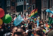 ÚLTIMA HORA: Jersey City inicia su mes del orgullo con eventos de verano Crowded street filled with people celebrating a lively Pride parade, waving rainbow flags and colorful balloons.