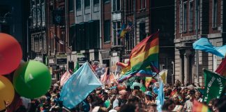 ÚLTIMA HORA: Jersey City inicia su mes del orgullo con eventos de verano Crowded street filled with people celebrating a lively Pride parade, waving rainbow flags and colorful balloons.