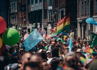 ÚLTIMA HORA: Jersey City inicia su mes del orgullo con eventos de verano Crowded street filled with people celebrating a lively Pride parade, waving rainbow flags and colorful balloons.