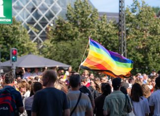 Vibrant pride parade scene with a waving rainbow flag amidst a diverse crowd outdoors.