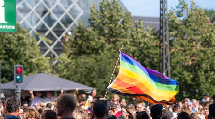 Vibrant pride parade scene with a waving rainbow flag amidst a diverse crowd outdoors.