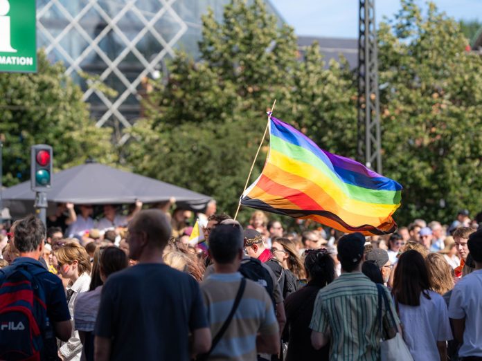 Vibrant pride parade scene with a waving rainbow flag amidst a diverse crowd outdoors.