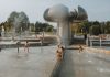 Happy children enjoy a sunny day playing in an urban fountain park with modern sculptures.