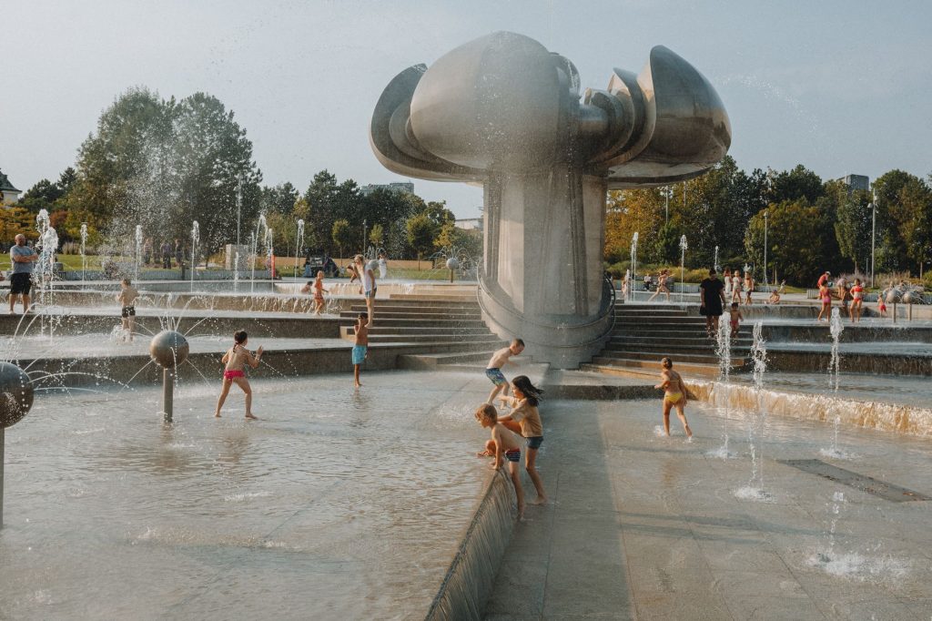 Happy children enjoy a sunny day playing in an urban fountain park with modern sculptures.
