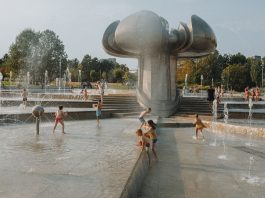 Happy children enjoy a sunny day playing in an urban fountain park with modern sculptures.