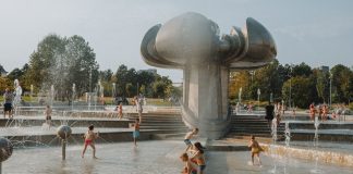 Happy children enjoy a sunny day playing in an urban fountain park with modern sculptures.