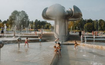 Happy children enjoy a sunny day playing in an urban fountain park with modern sculptures.
