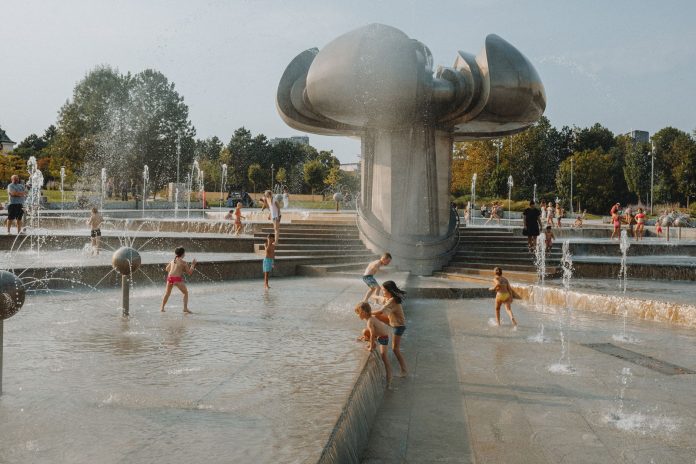 Happy children enjoy a sunny day playing in an urban fountain park with modern sculptures.