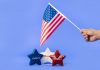 Hand holding American flag with red, white, and blue stars symbolizing liberty and freedom.