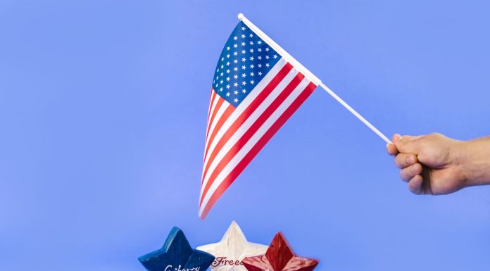Hand holding American flag with red, white, and blue stars symbolizing liberty and freedom.