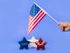 Hand holding American flag with red, white, and blue stars symbolizing liberty and freedom.