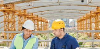 Engineering team analyzing blueprints together at an outdoor construction site with safety gear.
