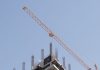 Tower crane working on a high-rise building construction site against a clear blue sky.