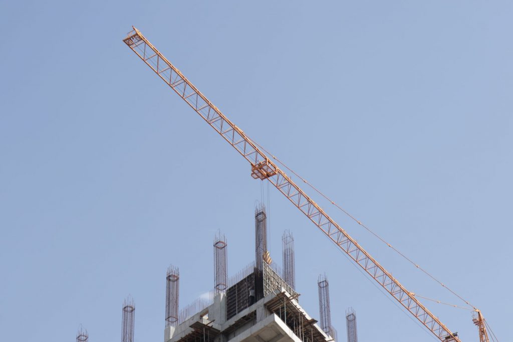 Tower crane working on a high-rise building construction site against a clear blue sky.