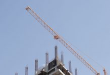 Tower crane working on a high-rise building construction site against a clear blue sky.