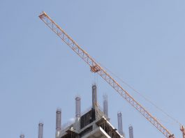 ÚLTIMA HORA: Torre de 56 pisos en Jersey City recibe préstamo de $220 millones Tower crane working on a high-rise building construction site against a clear blue sky.