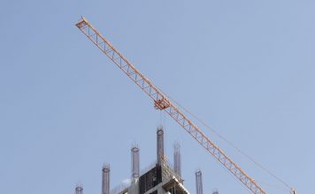 ÚLTIMA HORA: Torre de 56 pisos en Jersey City recibe préstamo de $220 millones Tower crane working on a high-rise building construction site against a clear blue sky.