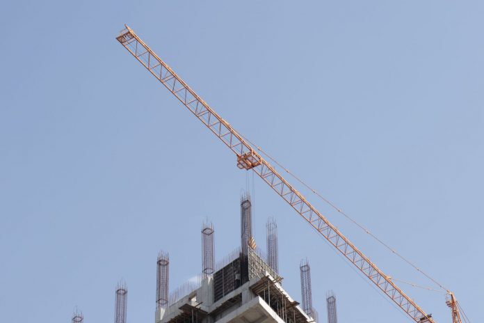 Tower crane working on a high-rise building construction site against a clear blue sky.