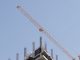 Tower crane working on a high-rise building construction site against a clear blue sky.