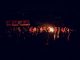 A large group of people gathered around a bonfire at night, featuring a vibrant outdoor atmosphere.