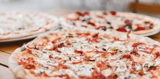 Close-up of freshly baked pizzas with mushrooms served on a wooden table.