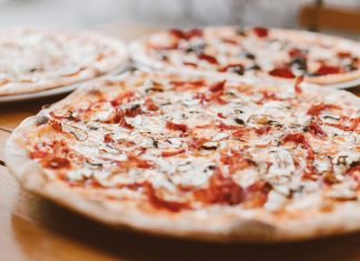 Close-up of freshly baked pizzas with mushrooms served on a wooden table.