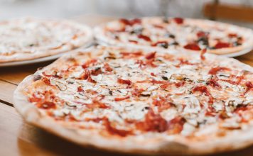 Close-up of freshly baked pizzas with mushrooms served on a wooden table.