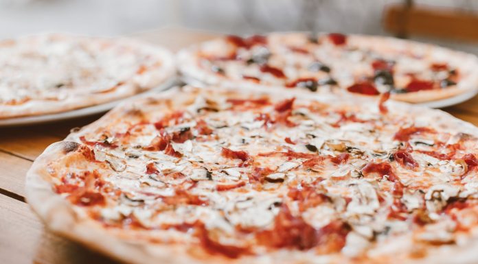 Close-up of freshly baked pizzas with mushrooms served on a wooden table.