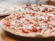 Close-up of freshly baked pizzas with mushrooms served on a wooden table.