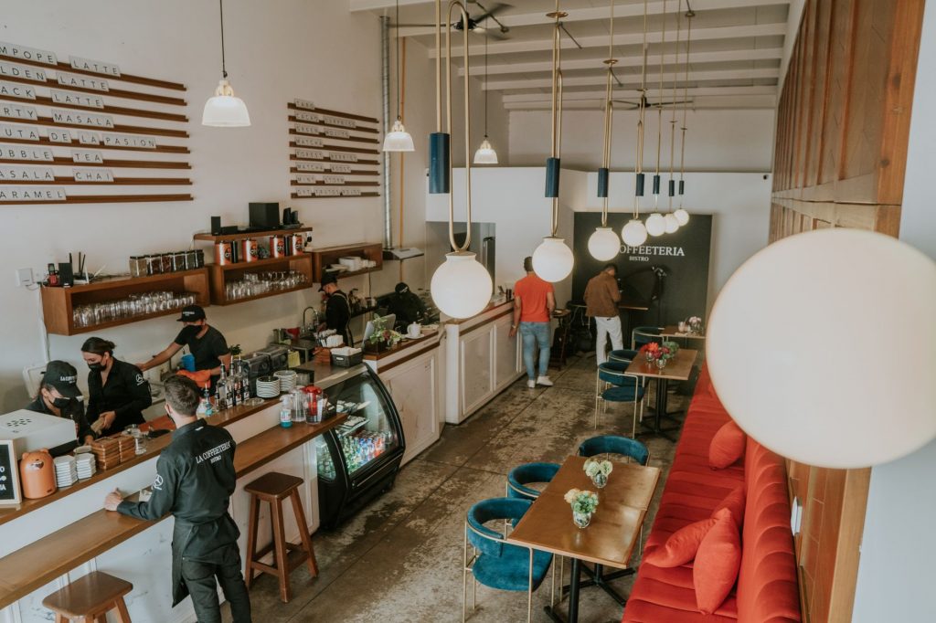Bright and inviting coffee shop interior with people working, featuring stylish decor and pendant lighting.