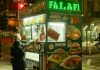 Vibrant street food scene in NYC with people ordering from a halal food cart at night.