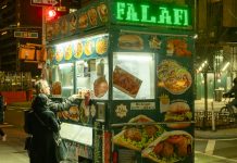 Vibrant street food scene in NYC with people ordering from a halal food cart at night.