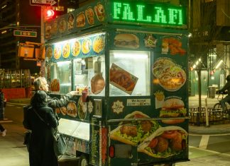 Vibrant street food scene in NYC with people ordering from a halal food cart at night.