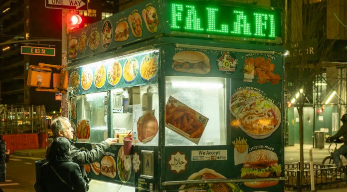 Vibrant street food scene in NYC with people ordering from a halal food cart at night.