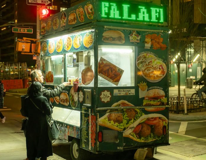 mejores-food-trucks-en-hoboken-2026 Vibrant street food scene in NYC with people ordering from a halal food cart at night.