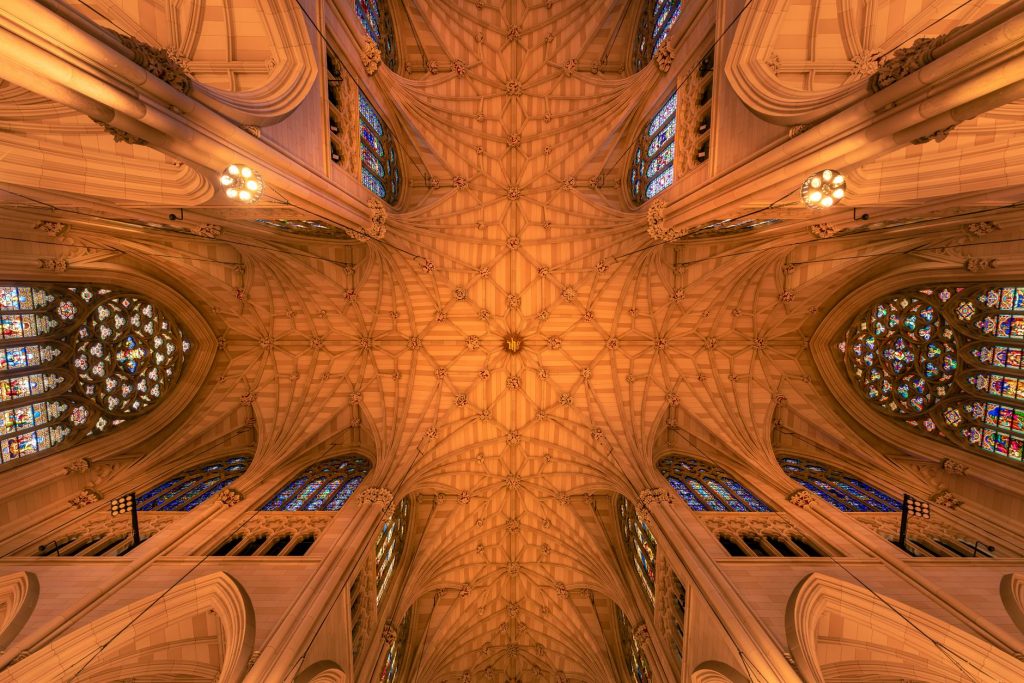 Intricate architecture and stained glass windows of St. Patrick's Cathedral ceiling in New York City.